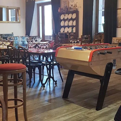 Salle de restauration avec des tables, chaises et tabourets en bois avec un baby-foot.