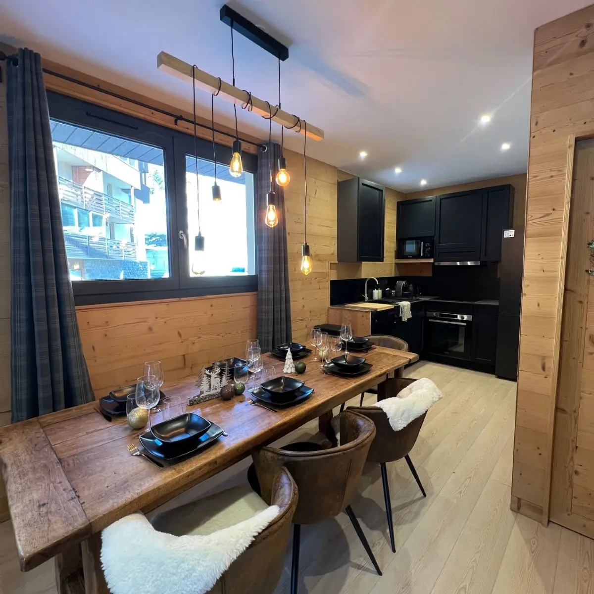 Bright living room with large dining table, modern kitchen area, wooden interior furniture, windows opening outside