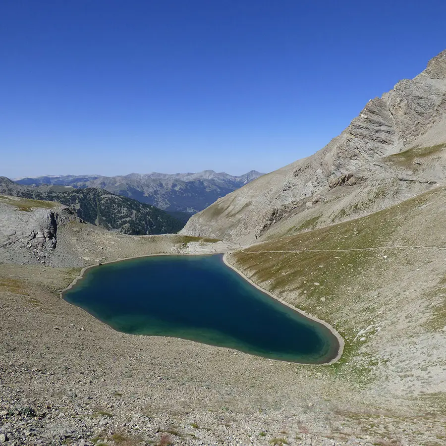 Lake Cayolle, a large body of water set amidst a rocky promontory with sparse vegetation. Mountains in the background