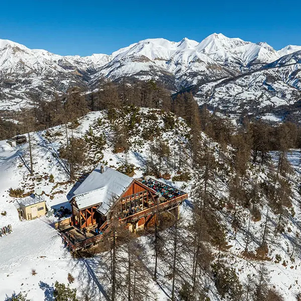 Vue du restaurant d'altitude en drone, chalet en bois et pierre au milieu des montagnes enneigées, terrasse en bois