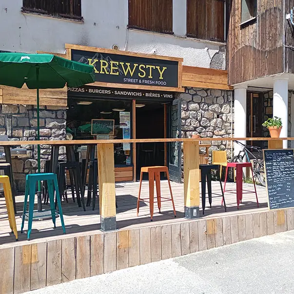 Vue de la terrasse extérieure en bois du restaurant, tabourets et chaises. Inscription Krewsty, street and fresh food'