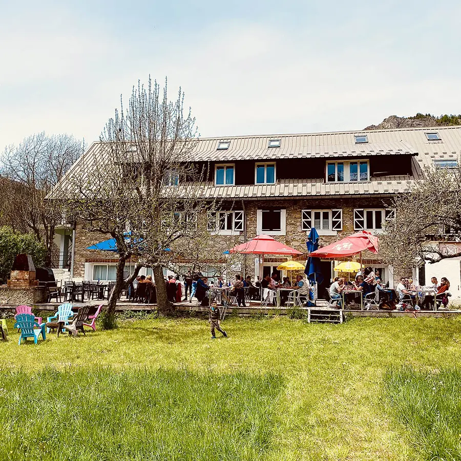 View of the restaurant in summer, a large 3-story stone building, outdoor terrace with tables and chairs, in a meadow setting