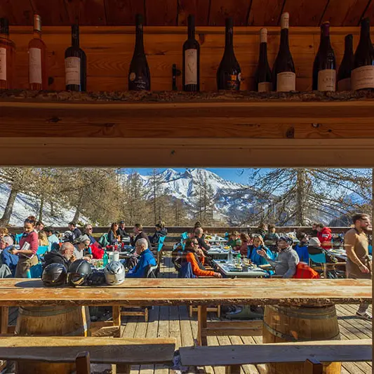 Terrasse du restaurant vue depuis l'intérieur, bois, tables et chaises, vue sur les montagnes enneigées en arrière-plan
