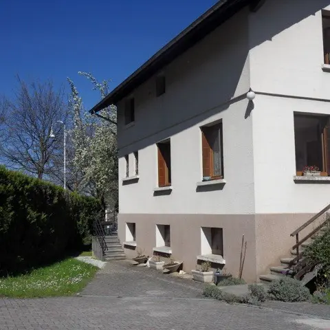 Cette maison individuelle, de construction traditionnelle, possède un étage et est dotée de fenêtres à volets en bois.