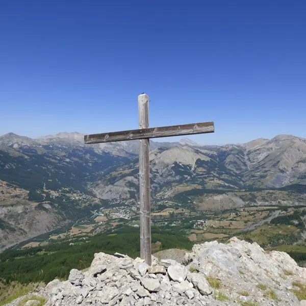 Croix de bois située au sommet de la montagne de Rochecline, sur un tas de cailloux. Vue complètement dégagée du village d'Allos et des montagnes en contrebas