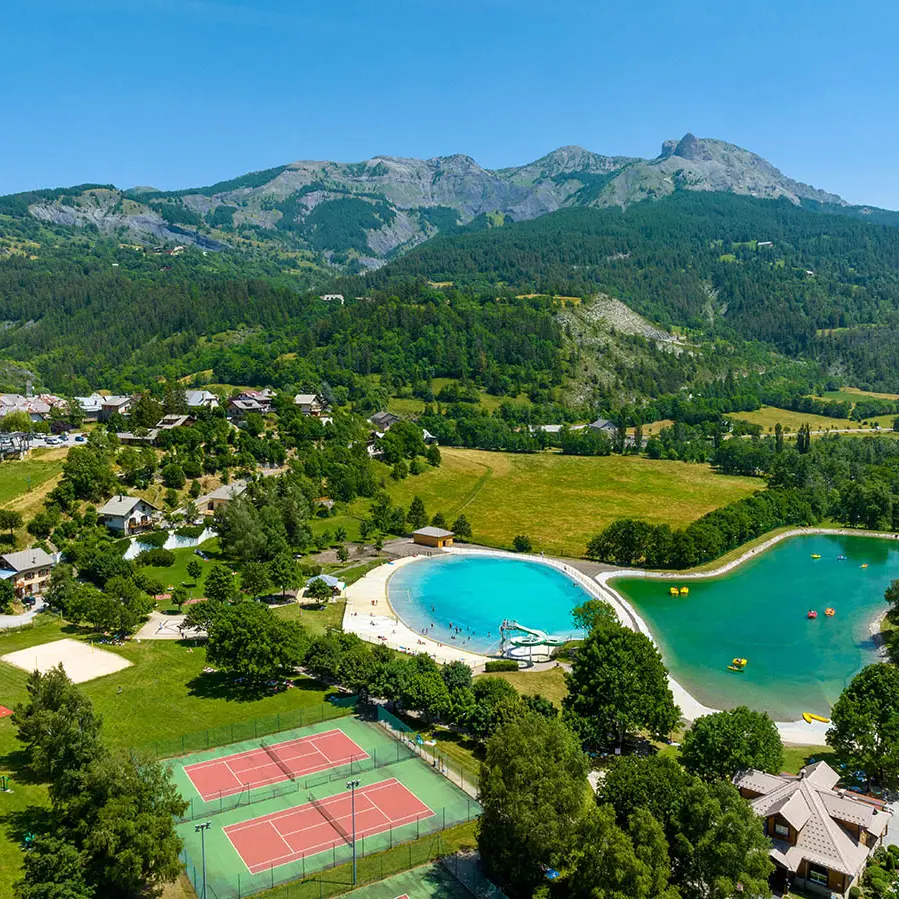 Parc de loisirs d'Allos depuis un point haut : deux grands bassins d'eau pour les pédalos et la baignade, dans un écrin de nature situé à côté du village. A côté des bassins, on trouve deux terrains de tennis, un terrain de volley-ball, et des jeux pour enfants