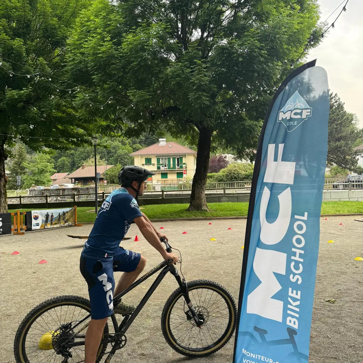 moniteur guide sur son vélo à coté d'un drapeau MCF