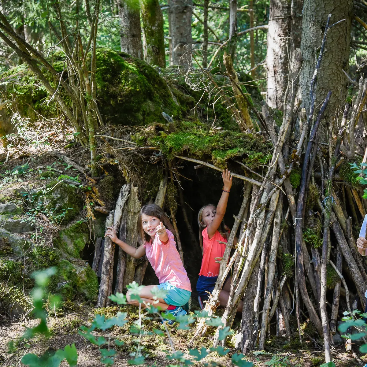 3 enfants en train de construire une cabane avec des branches d'arbre
