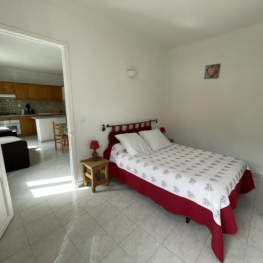 Chambre à coucher lumineuse avec lit double, sol carrelé, ameublement bois, porte vers séjour