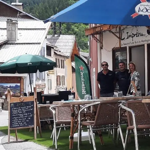 Terrasse extérieure du restaurant dans la grand-rue d'Allos, fausse pelouse, tables et chaises, parasols