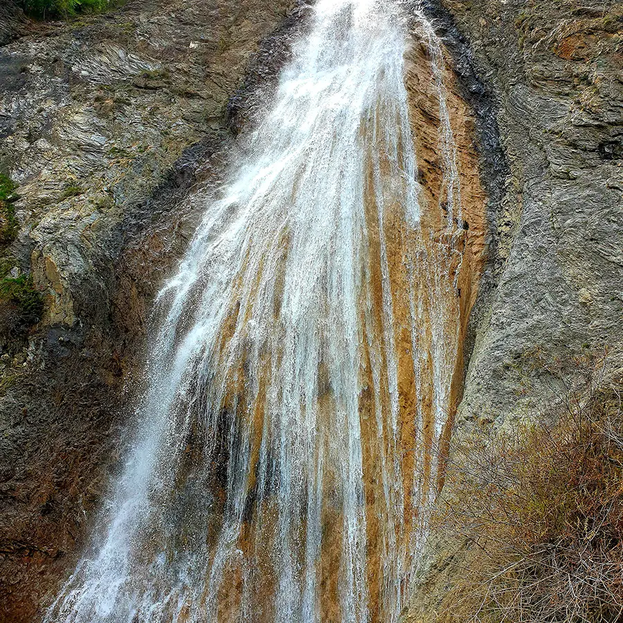 Cascade de Chaumie, cascade rocheuse se déversant depuis une forêt de conifères dans un petit bassin naturel creusé dans la roche