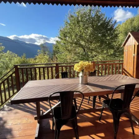 Wooden terrace with a wooden table and iron chairs, small wooden garden shed. Mountain view.