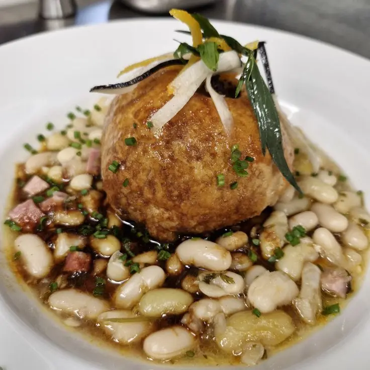 La tourte au foie gras du chef déposé sur des haricots mogettes dans une assiette blanche.