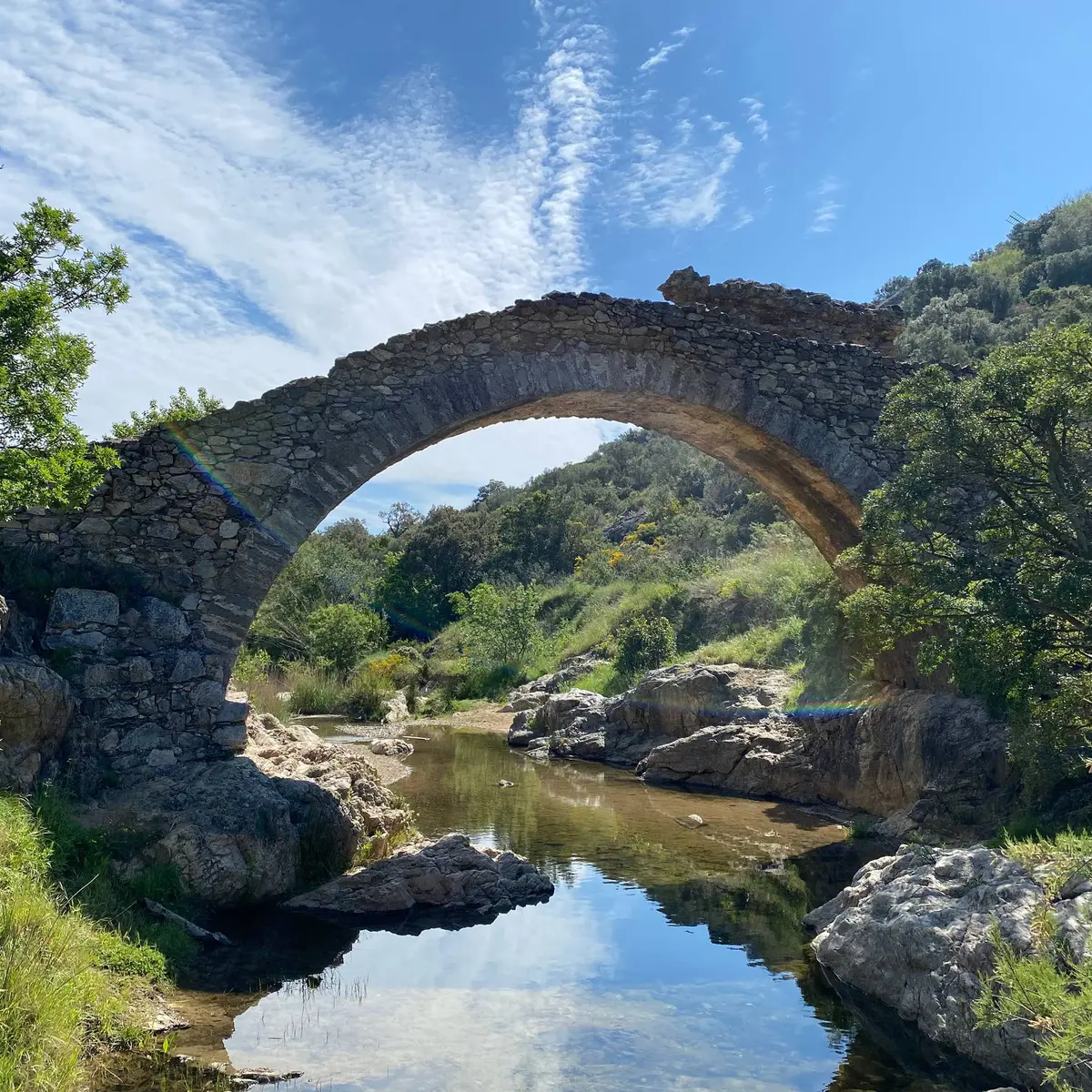 Pont en pierres apparentes enjambant une petite rivière entouré de végétation méditerranéenne