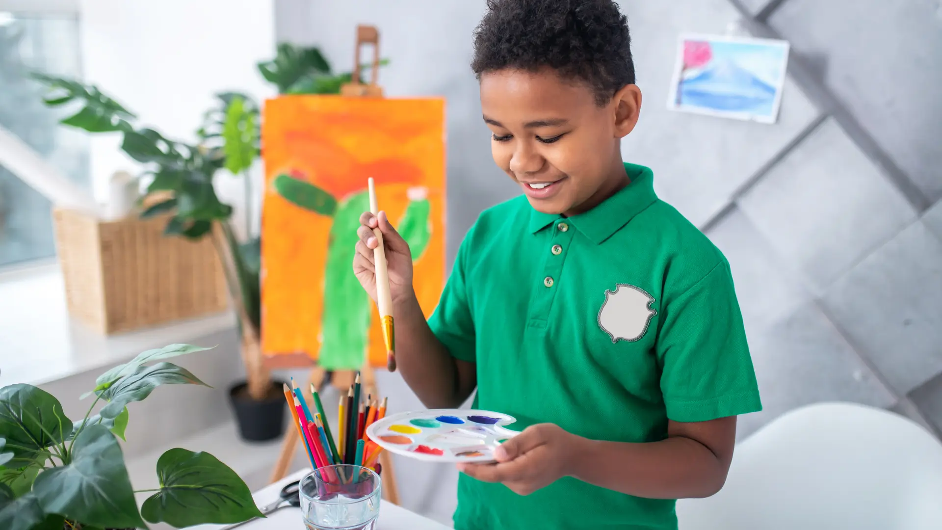 Boy looking holding paintbrush over palette with paints