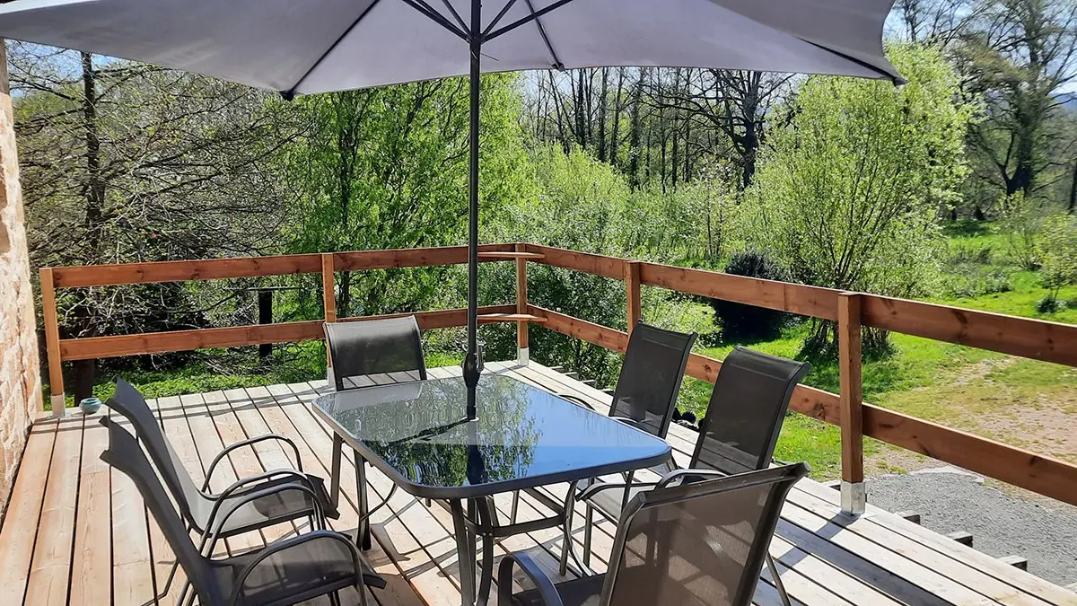 La terrasse du gîte, la rivière est au fond, juste derrière les grands arbres.