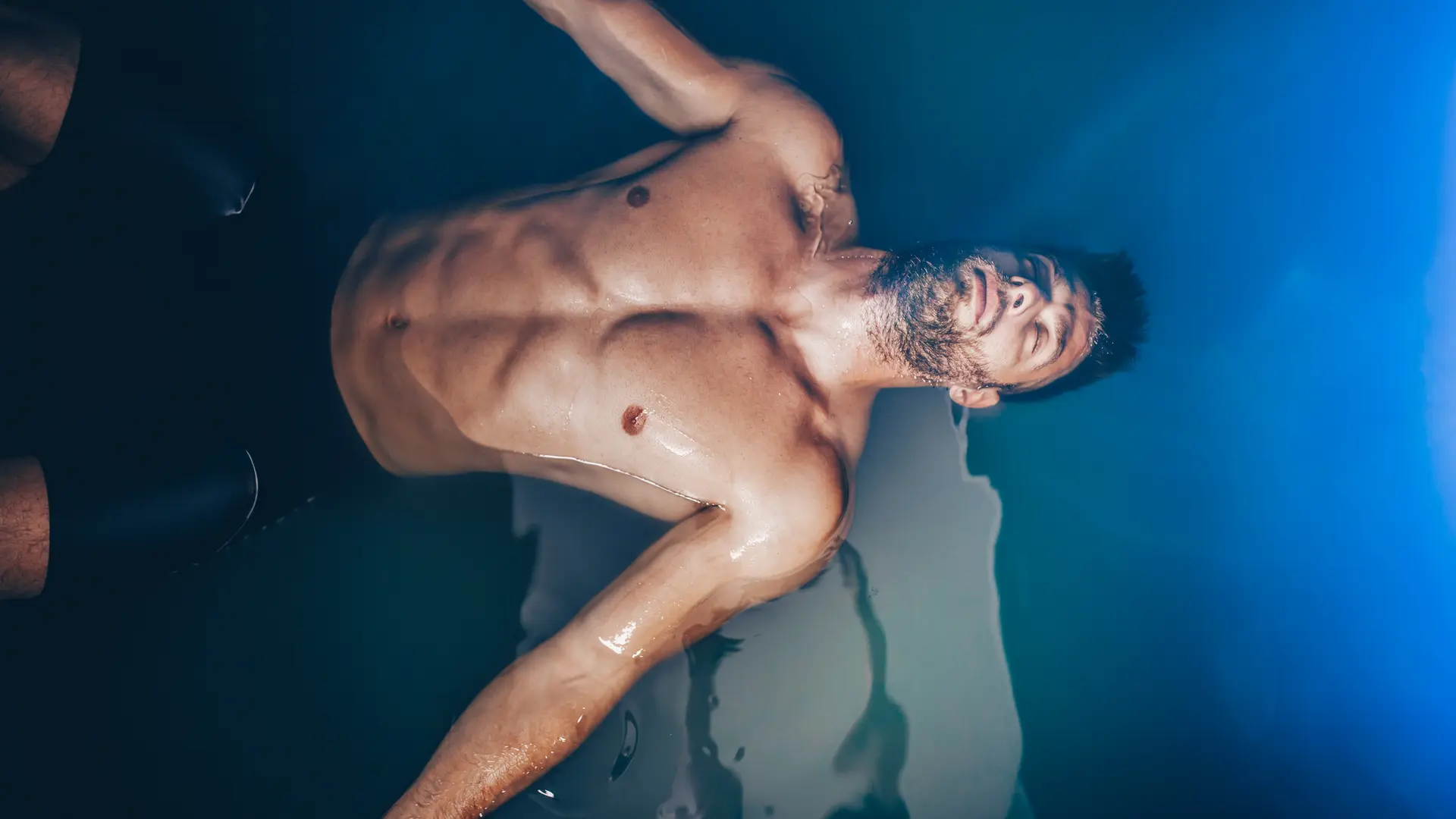 Handsome beard man floating in tank filled with dense salt water used in meditation, therapy, and alternative medicine.