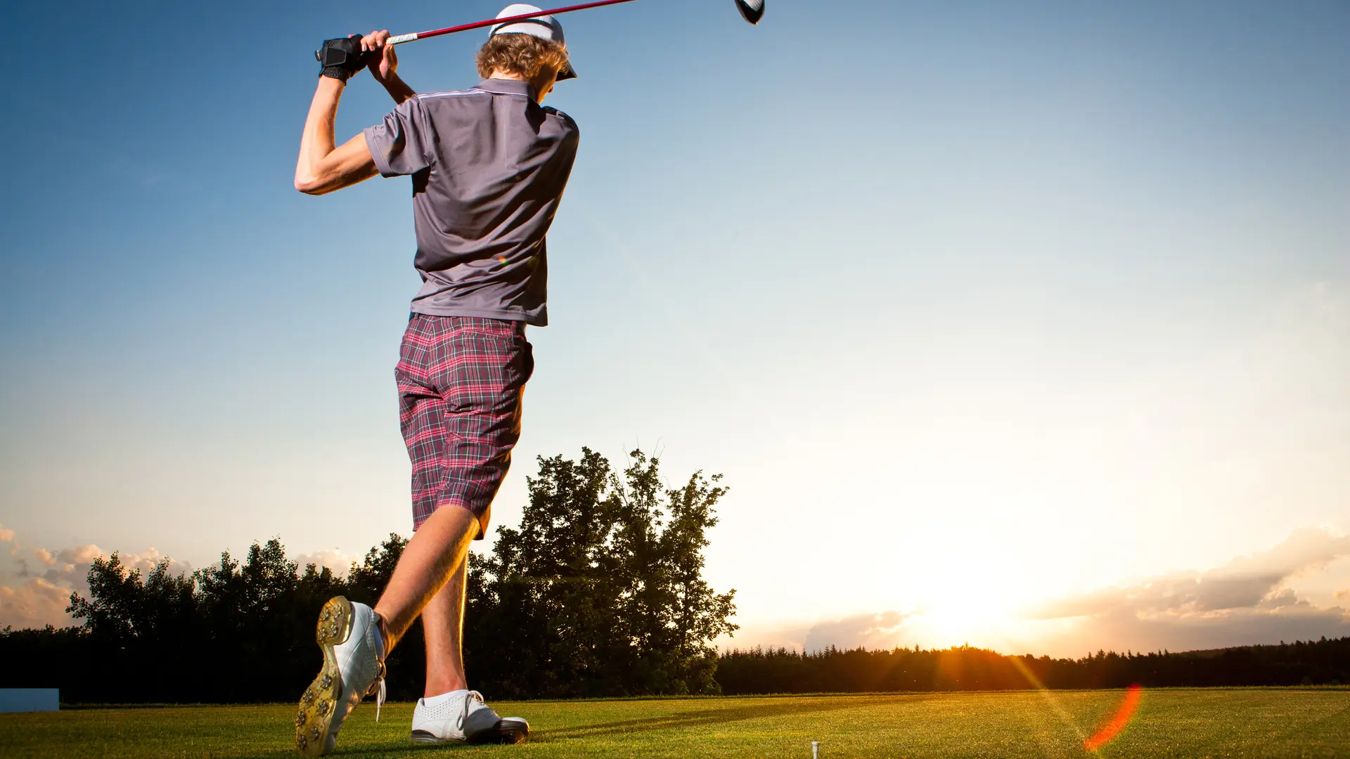 Male golf player teeing off golf ball from tee box to beautiful sunset