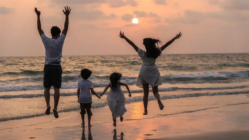 Asian young happy family enjoy vacation on beach in evening. Dad, mom and kid relax running together near sea while silhouette sunset. Lifestyle travel holiday vacation summer concept.