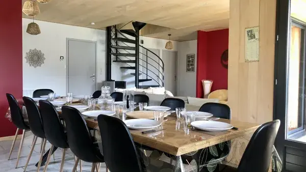 Le coin repas et la cuisine avec accès direct sur la terrasse couverte ; à gauche, l'entrée de la maison ;  près de l'escalier, le garage ;  au fond à droite, le salon, les toilettes, les 2 chambres du rez-de-chaussée et la salle de bain.