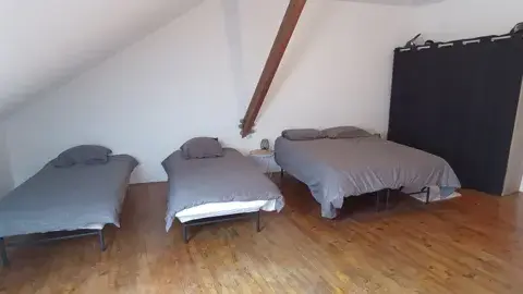Chambre spacieuse sous les combles avec un lit double et deux lits simples, idéale pour les familles ou groupes.