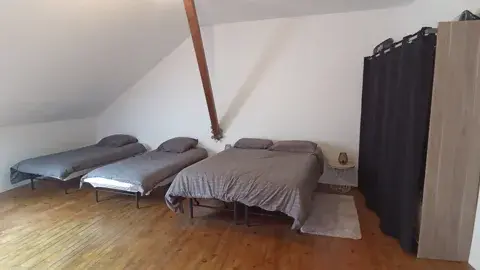 Chambre sous combles avec un lit double et deux lits simples, offrant confort et espace pour plusieurs personnes.