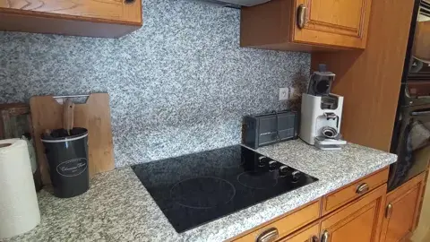 Cuisine équipée avec plan de travail en granit, four, machine à café et accessoires pratiques pour préparer vos repas.