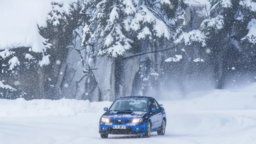 montre une voiture de rallye bleue en pleine action sur un circuit entièrement recouvert d'une épaisse couche de neige blanche.