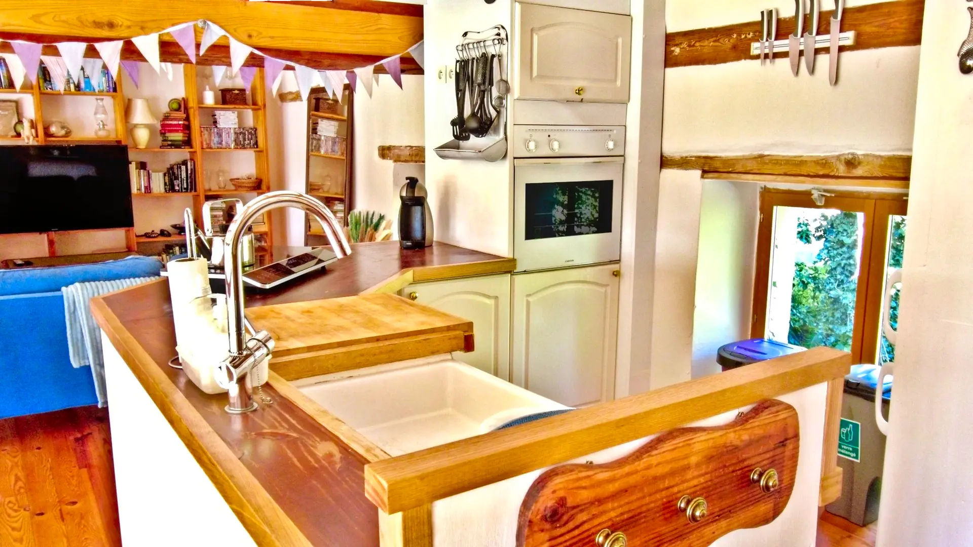 La cuisine se trouve entre la salle à manger et le salon de la mezzanine. Une petite cuisine américaine avec le nécessaire pour cuisiner. Le bar en bois est de forme octogonale ouvert avec un évier, une table à induction et sa bouilloire et contre le mur, une machine à café. On aperçoit des ustensiles de cuisine accroché à un support ancien détourné. A droite, une niche avec une étagère comprenant trois théières. En dessous, il y a un micro-onde et une réfrigérateur (frigo et une partie congélation). Au dessus de la fenêtre, on trouve un support magnétique pour ranger les couteaux de cuisine. La luminosité de la mezzanine est apportée par la lumière traversante venant des fenêtres.