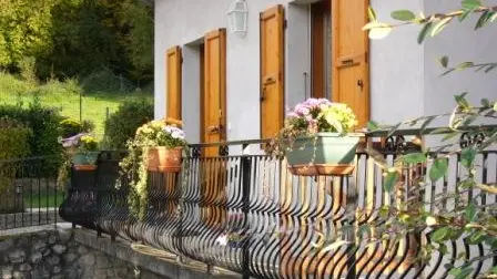 Il s'agit d'une maison individuelle. Un balcon avec une balustrade métallique et des plantes en pots est attenant à la maison. Les fenêtres sont équipées de volets en bois.