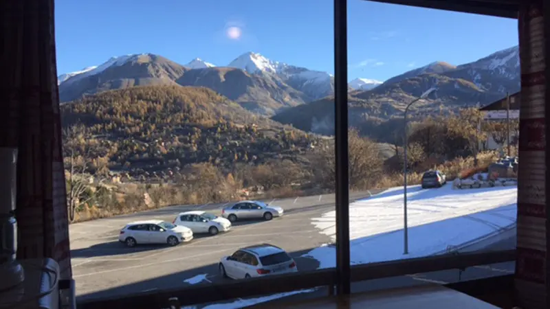 Bright room opening onto the outside, wooden furniture, large window, view of the snow-capped mountains