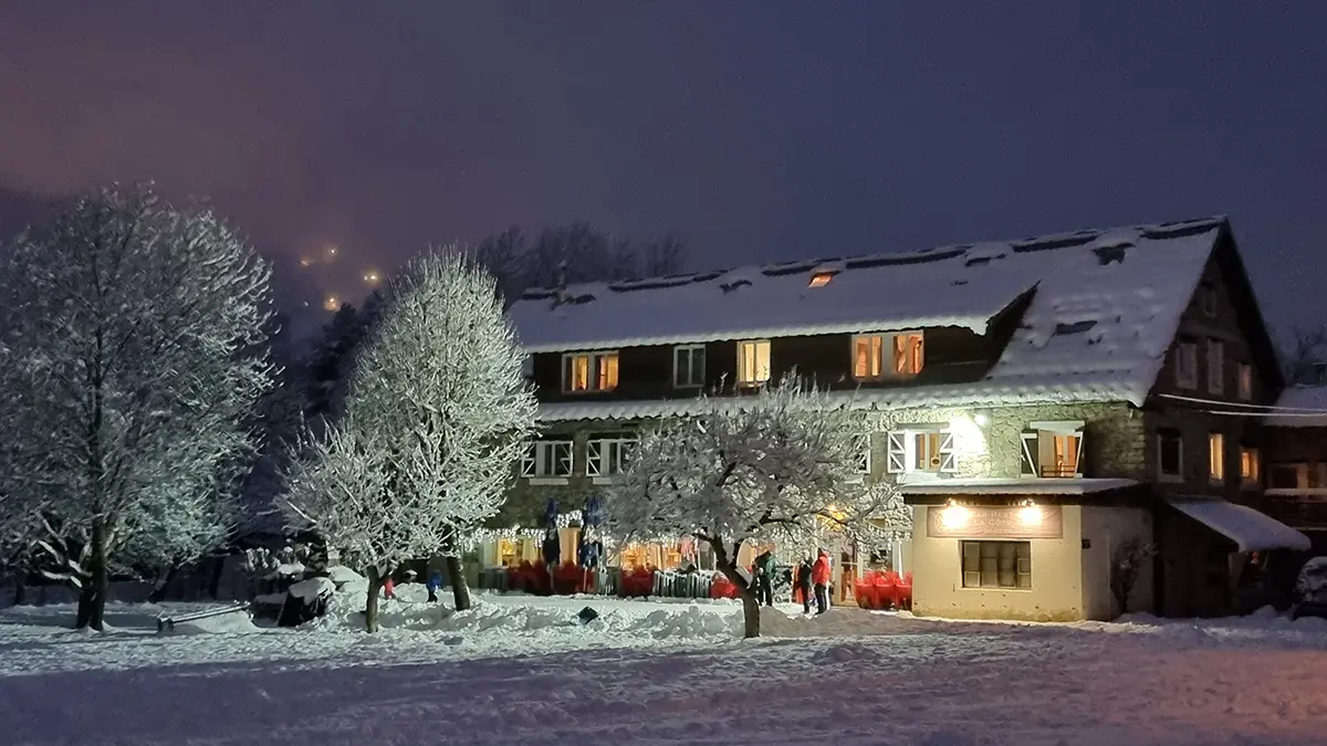 View of the restaurant in winter, a large 3-story stone building, outdoor terrace, at the back of a snowy meadow