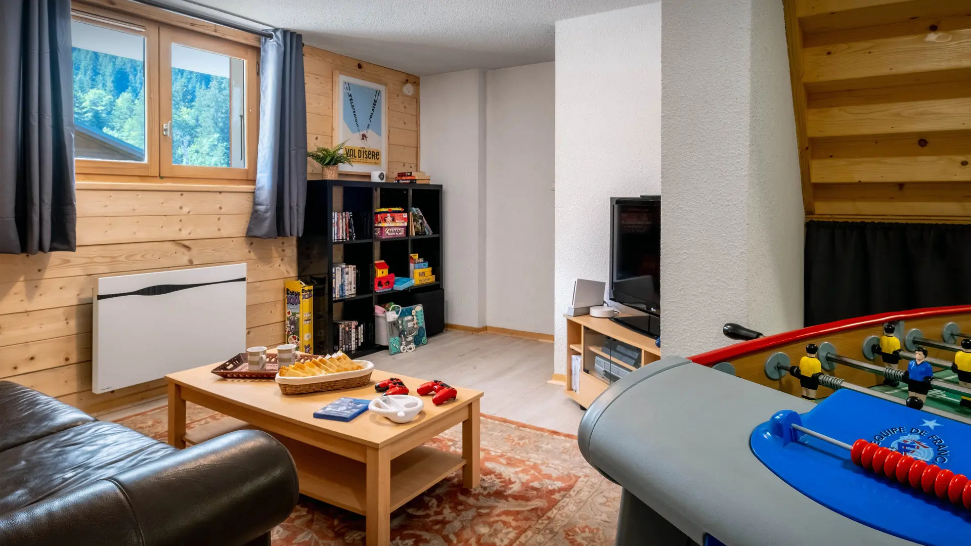 Salle de jeux avec canapé, table basse, baby foot, télévision, jeux pour enfants