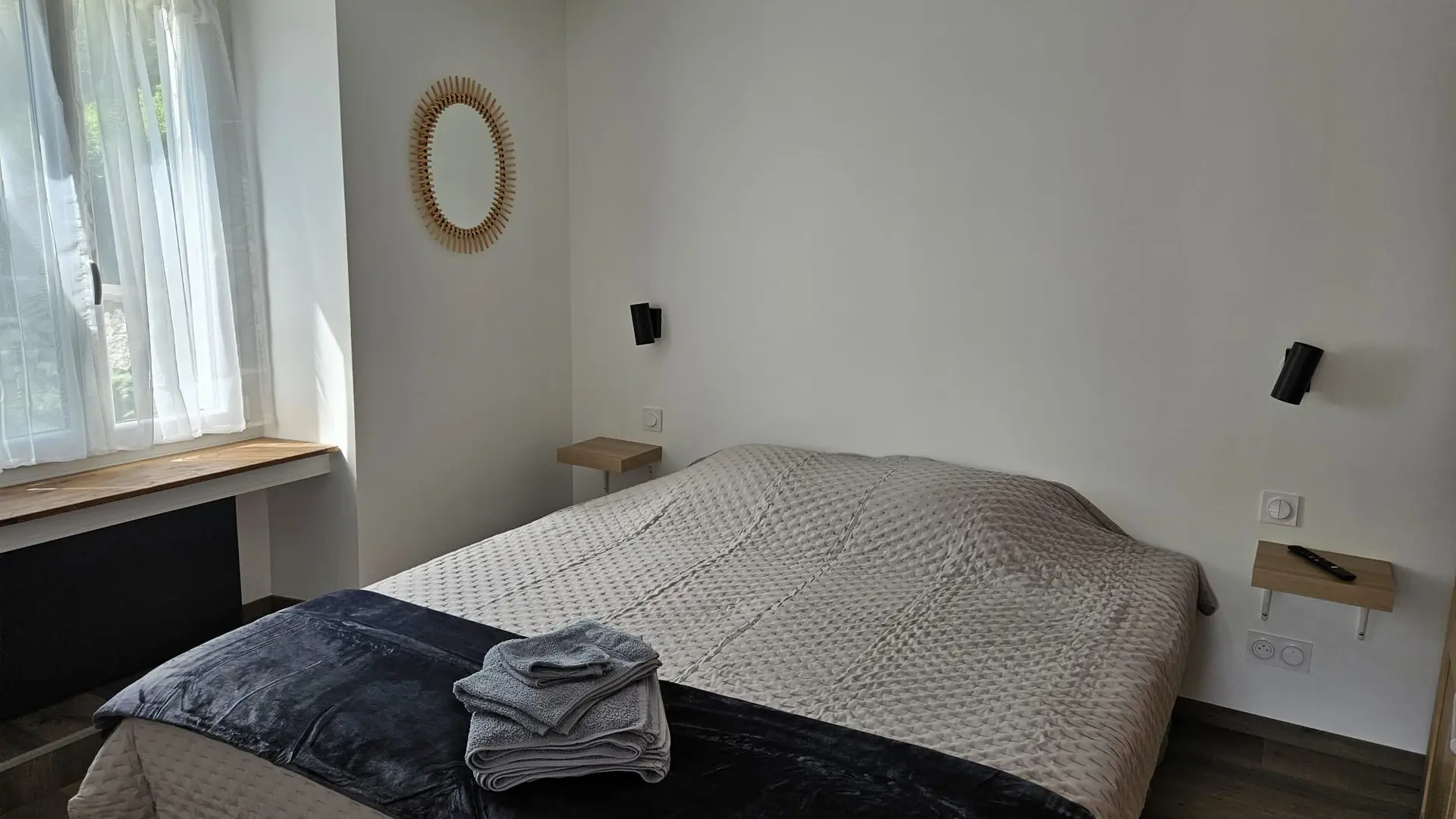 Chambre avec un lit double, deux tables de nuit, un miroir rond et un radiateur.