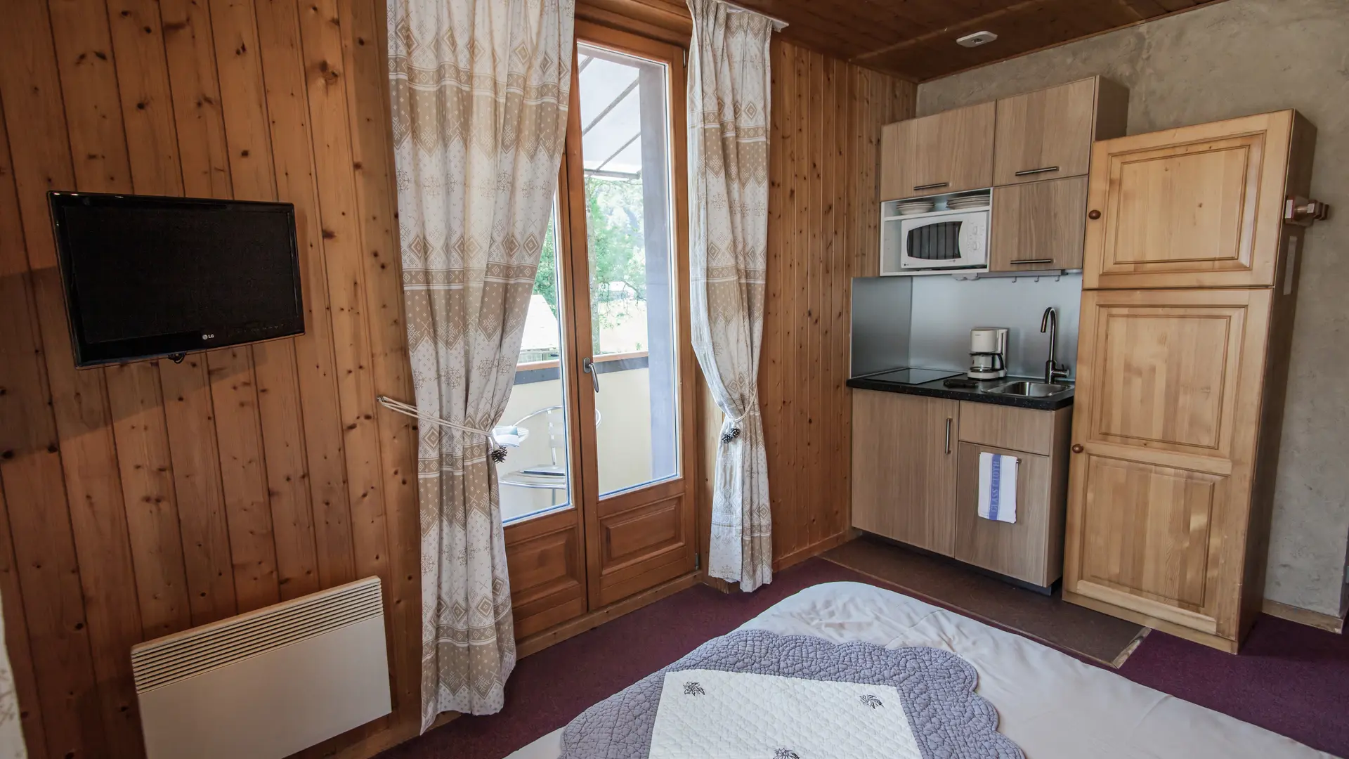 Vue sur le lit, la télévision, l'armoire, la cuisine et le balcon