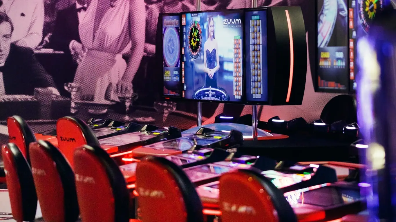 La salle de jeux du casino JOA d'Uriage est un espace lumineux et coloré, rempli de machines à sous aux designs variés et de jeux vidéo interactifs, créant une ambiance animée et festive.