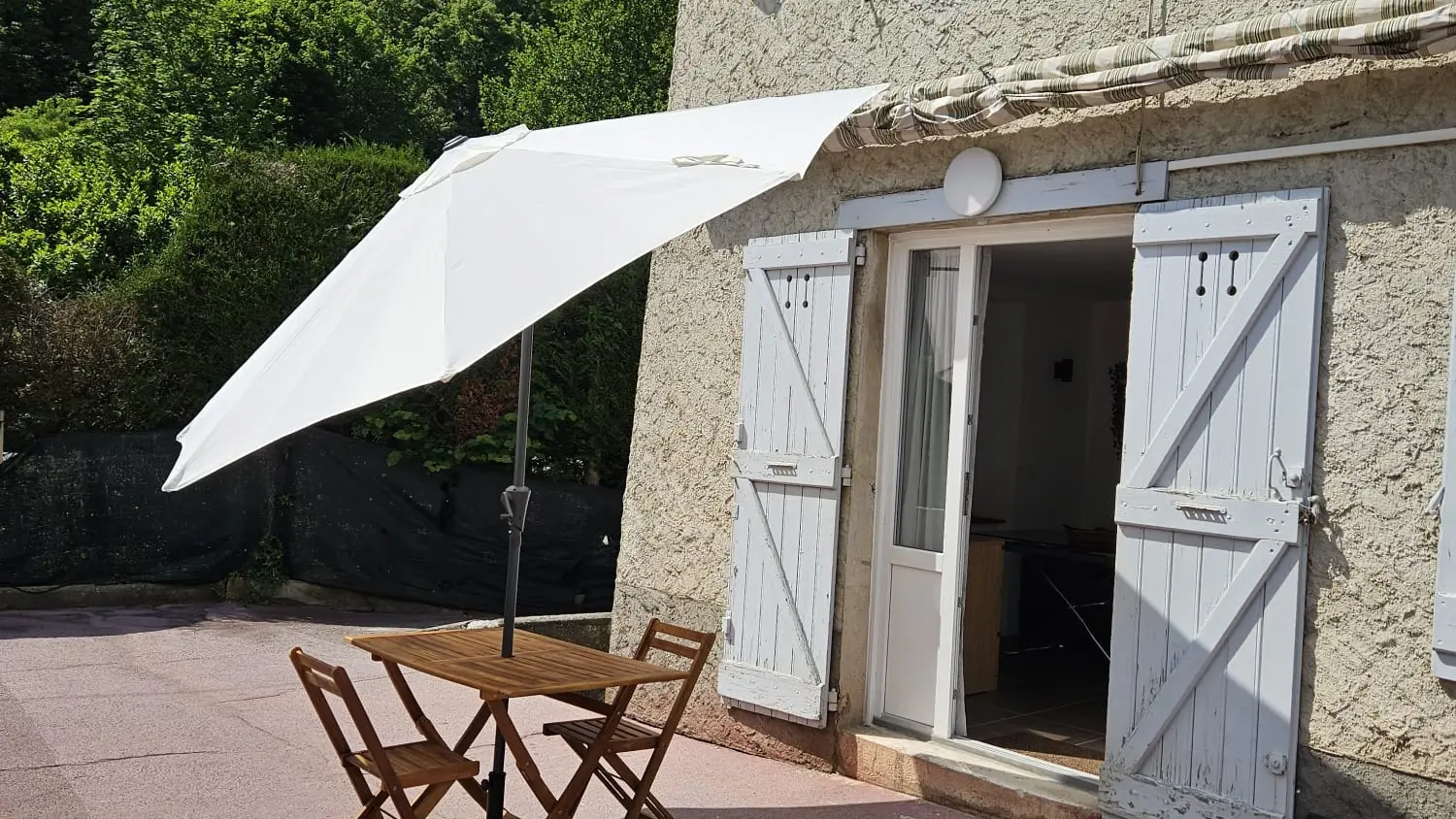 Terrasse extérieure avec une table et des chaises, abritée par un parasol et adjacente au gite.