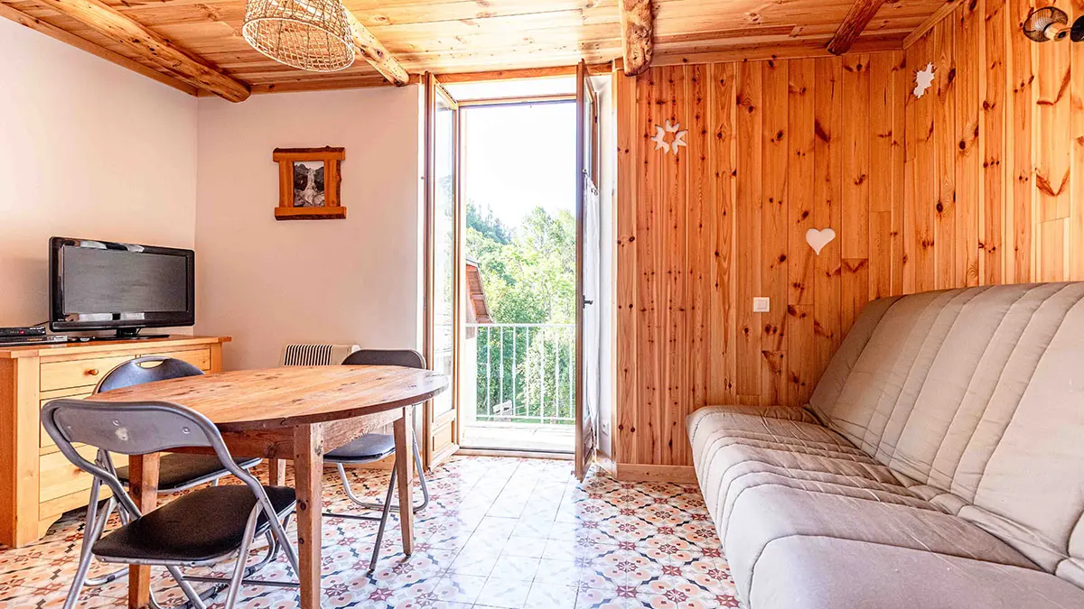 Bright living room with sofa, television, dining table, wooden furniture, tiled floor, French windows