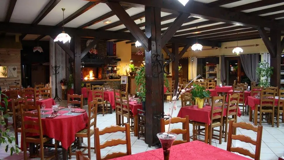 Vous vous trouvez dans une pièce spacieuse, avec un plafond haut soutenu par des poutres en bois. Des tables rondes, séparées par des chaises en bois, occupent la majeure partie de l'espace.