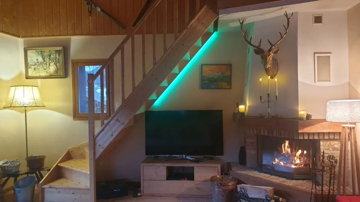 Salon d'appartement avec cheminée, TV, fenêtre, ameublement bois, escalier vers l'étage supérieur