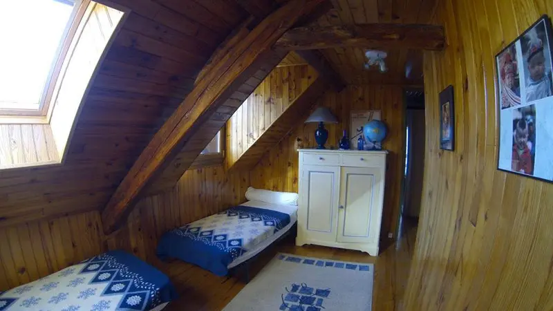 Bright bedroom with high ceilings, two single beds, wooden furniture, parquet flooring, and a skylight.