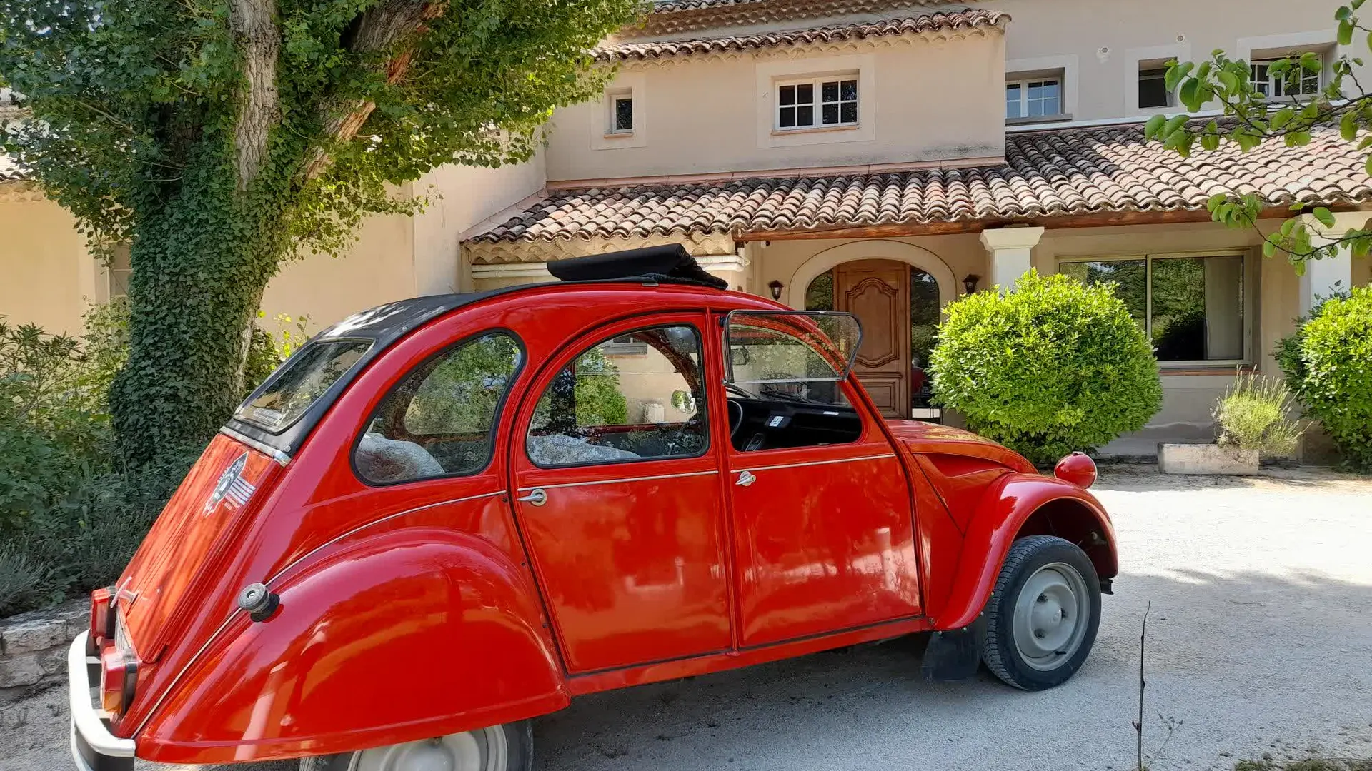 Une 2CV rouge emblématique stationnée devant une maison provençale au charme authentique.