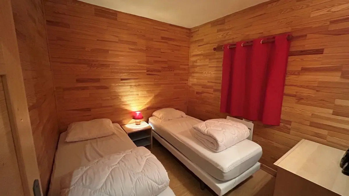 Bedroom with two single beds, wooden furniture, parquet flooring, window