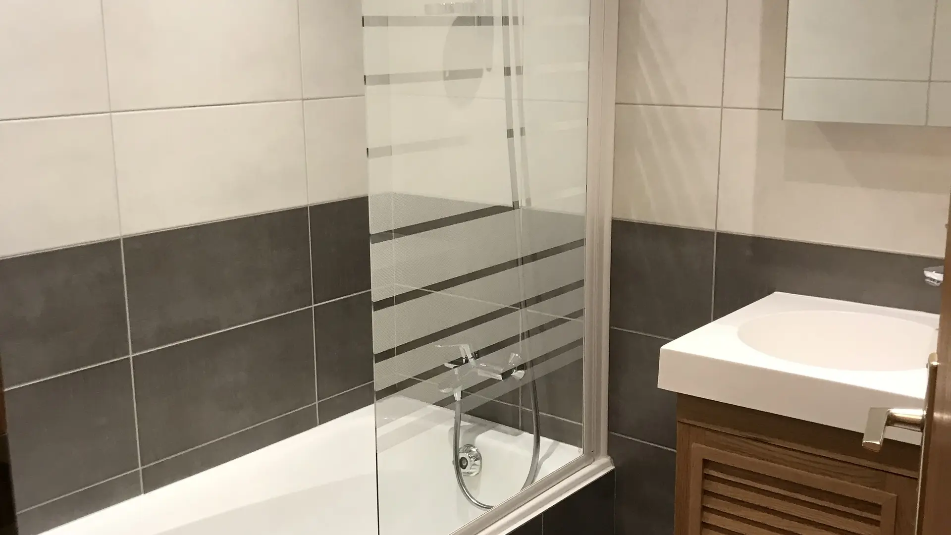 Salle de bains avec sa baignoire/douche, vasque et son meuble, miroir