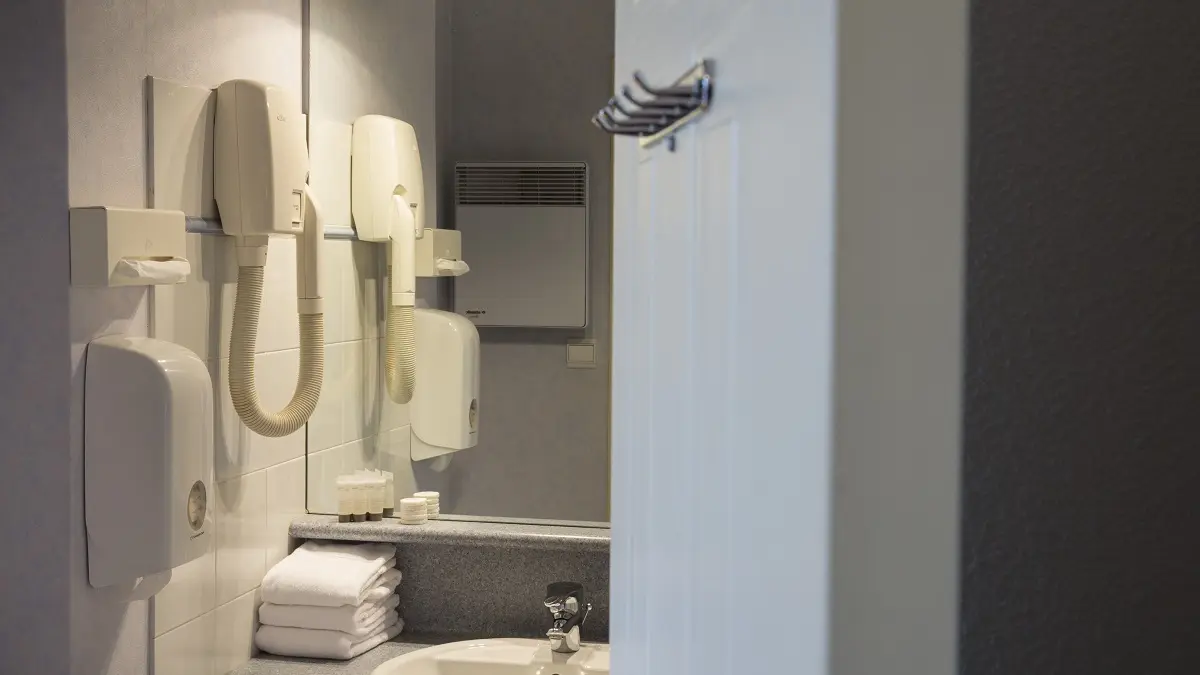 Salle de bain en marbre gris avec un lavabo blanc et quelques serviettes soigneusement pliées et d'un sèche-cheveux..