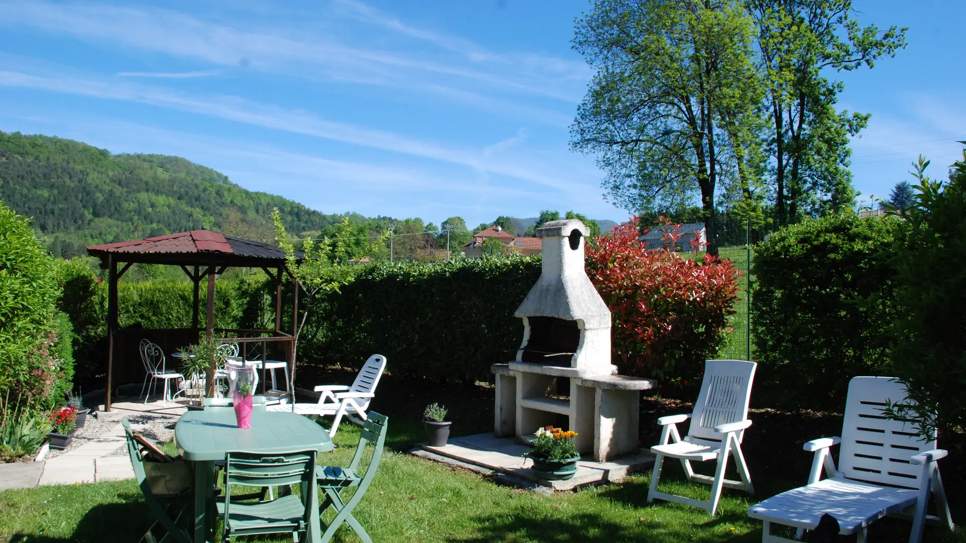 Ce jardin extérieur dispose d'une pelouse, d'un barbecue en dur et d'un coin salon avec des meubles de jardin. Une tonnelle apporte de la fraîcheur à cet espace.