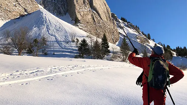 Skieur montant dans une prairie enneigée devant une falaise