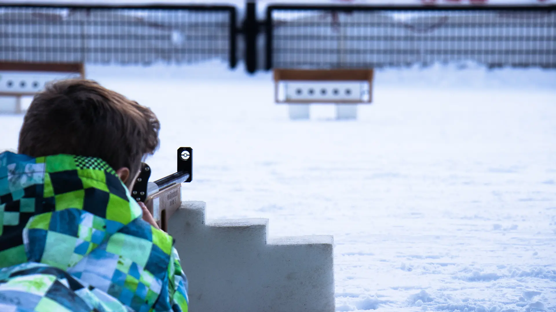 Un jeune garçon s'initie au tir de précision en visant des cibles de biathlon avec une carabine laser. Allongé dans la neige.