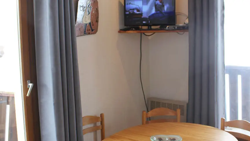 Bright living room with dining table, TV, windows and curtains, wooden balconies