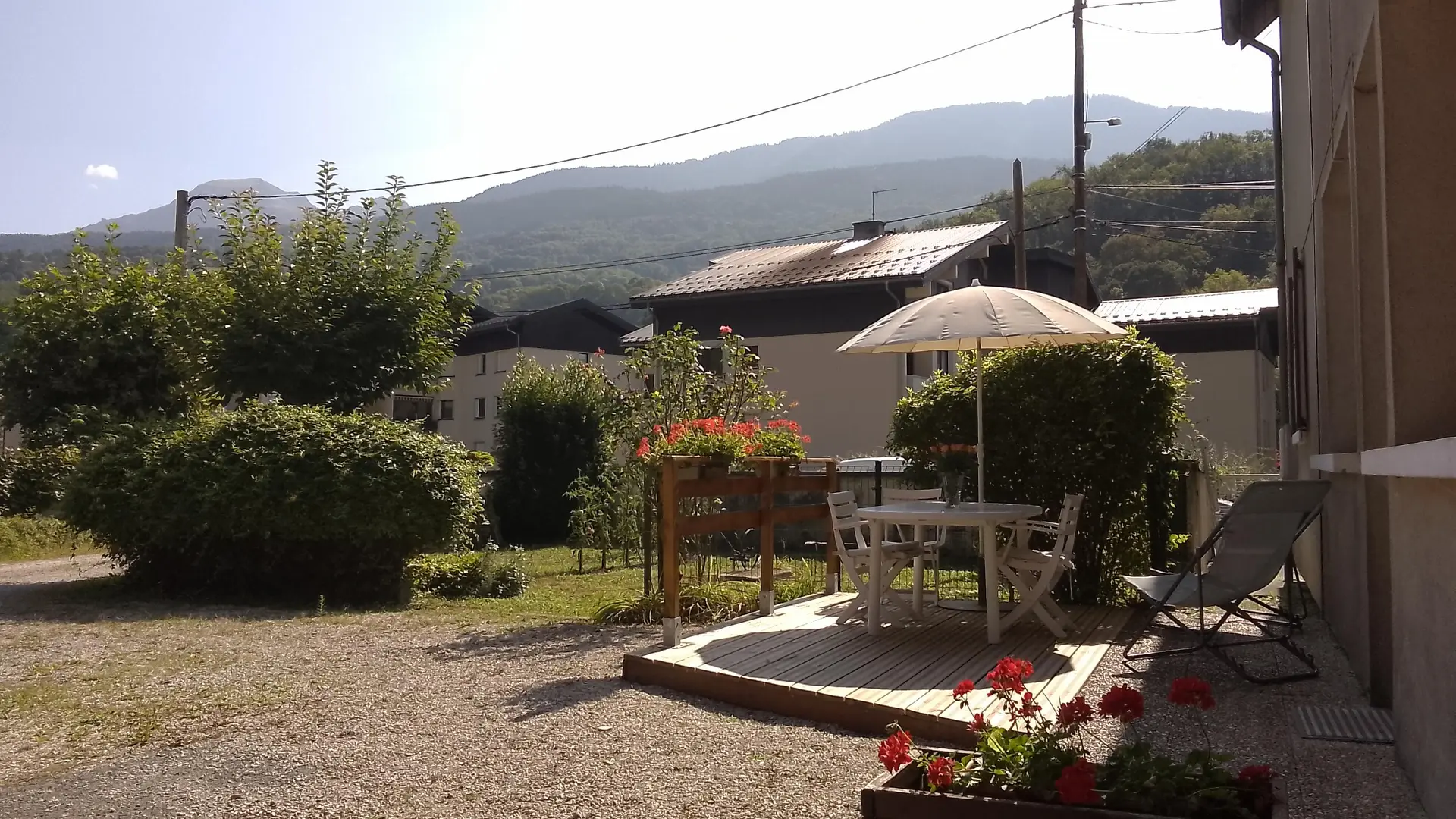 La terrasse, aménagée avec du mobilier de jardin, offre une vue dégagée sur un jardin verdoyant et un paysage montagneux.